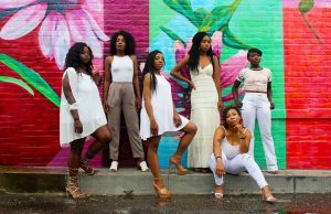 Six black women standing in front of multicolored wall with flowers