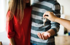 women in red shirt and man in blue stripe shirt handed house key