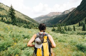 woman with yellow backpack on green mountains