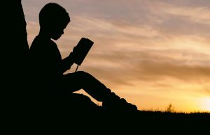 silhouette of child reading by sunset