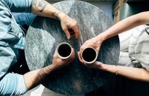 two people holding coffee on a grey table