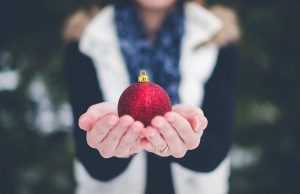 person in white vest holding red christmas ornament