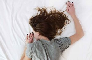 woman in grey shirt face down on white bed