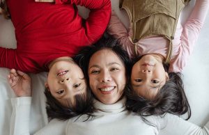 asian woman in white sweater laying with two asian children in red sweater and pink shirt