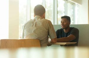 black man in black shirt sitting at wood table with white man in white shirt