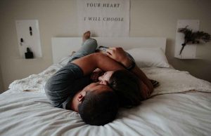 man and woman hugging and laying down on white bed with white posters