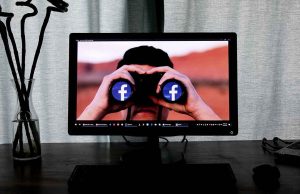 computer screen with man holding binoculars with facebook logo