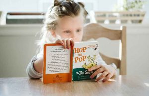 child with braided hair reading hop and pop at a wood table