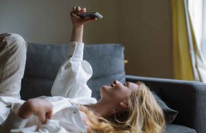 woman in white blouse and khaki pants holding phone on couch