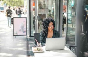 woman with black curly hair in black blazer working outside on laptop