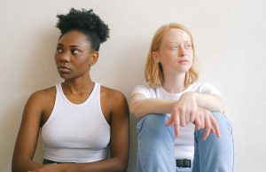 black woman in white tank top sitting next to white woman in jeans and white shirt