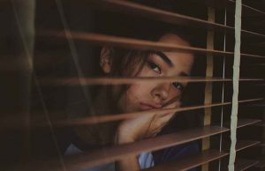 woman looking out window with wooden blinds